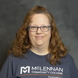 Smiling person wearing a McLennan Community College T-shirt against a gray studio background.
